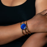 A beautifully handcrafted gold-toned cuff bracelet with a colorful glass stone in the center. Model is wearing the blue stone bracelet.